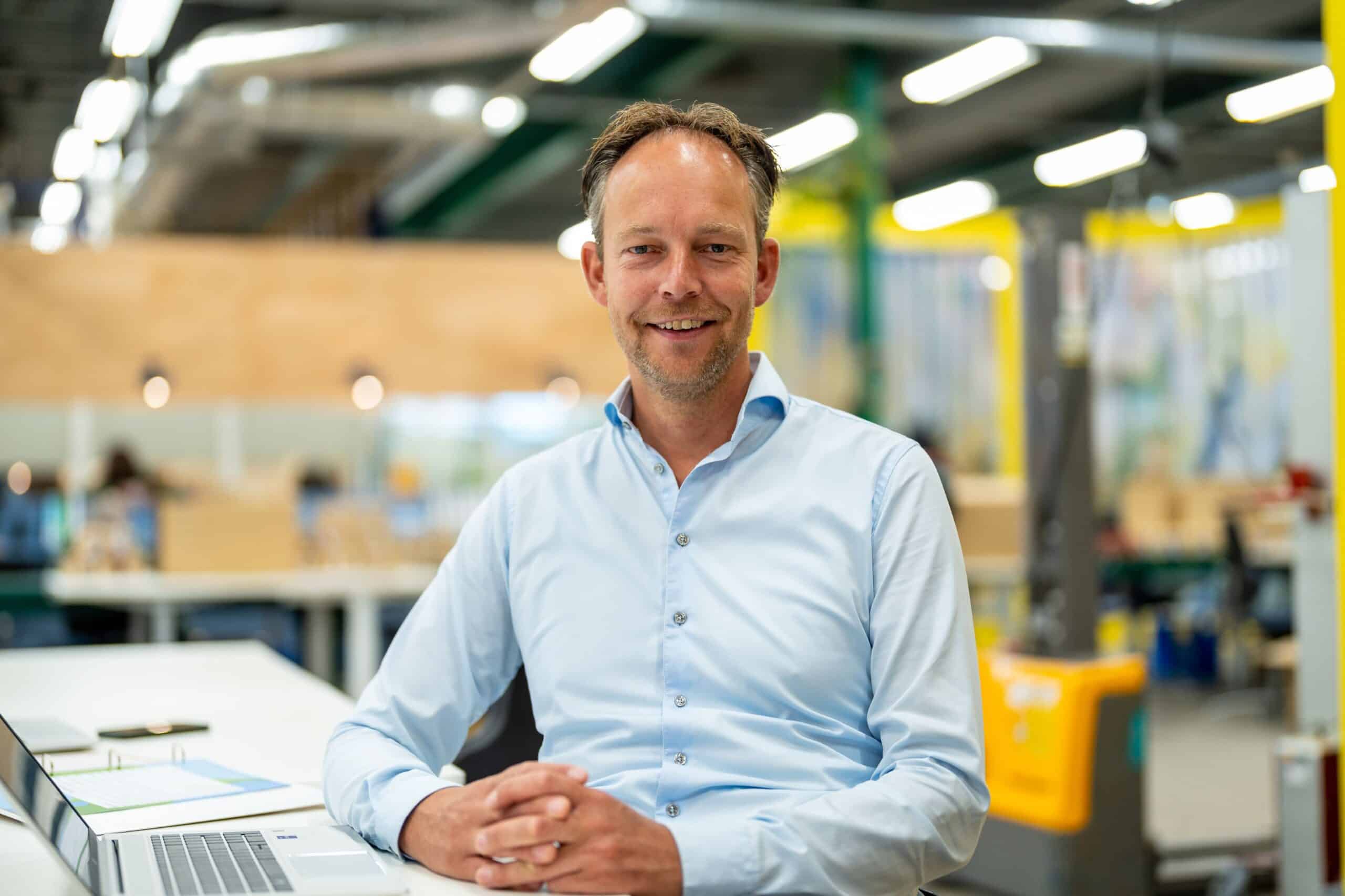 Glimlachende zakenman in lichtblauw overhemd op moderne kantoorlocatie met laptop en industriële achtergrond